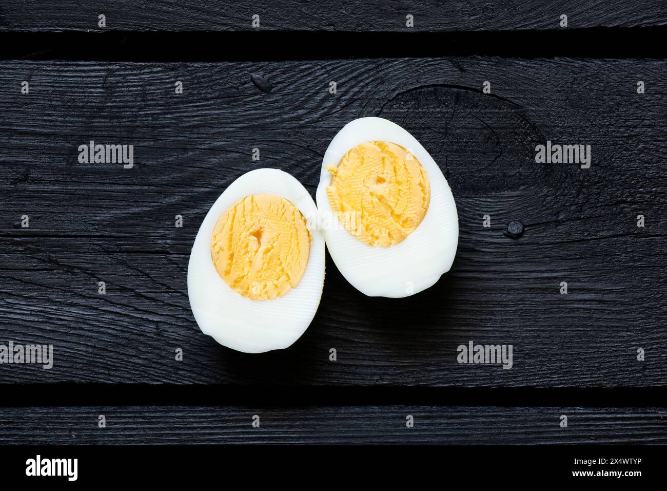 Un uovo di pollo bollito, tagliato, giace su un bordo di legno nero, cibo Foto Stock