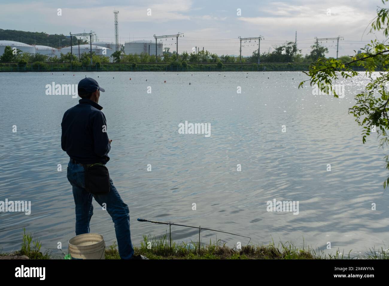 Un uomo pesca in un lago della città. Atmosfera urbana sulla riva del lago Foto Stock