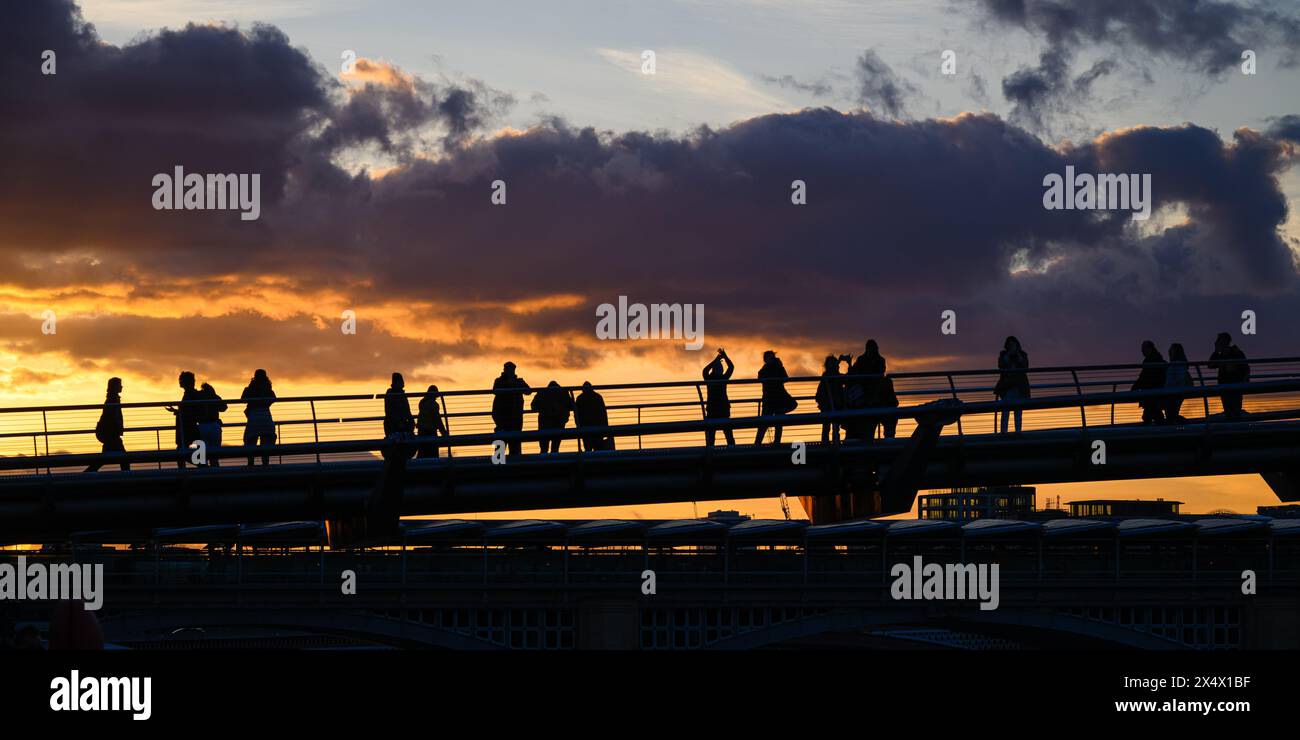 Sagome di persone sul Millennium Bridge che guardano il tramonto arancione sulle nuvole nel centro di Londra Foto Stock