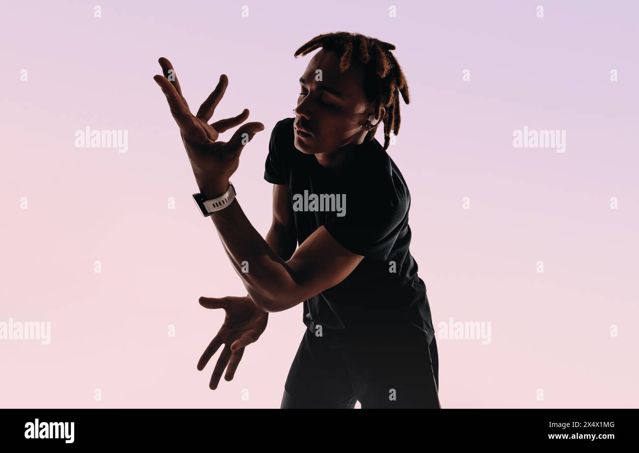 Il giovane balla energicamente in una silhouette da studio, esprimendo se stesso attraverso movimenti ritmici. Ascolta musica a occhi chiusi e auricolari Foto Stock