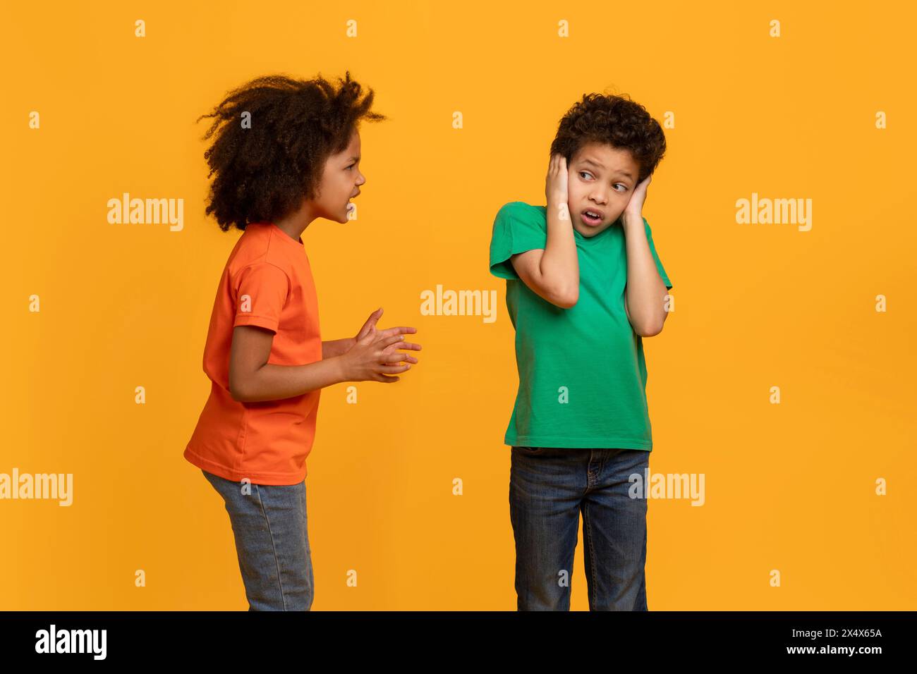 Young Boy copre le sue orecchie mentre Girl parla, sfondo giallo Foto Stock