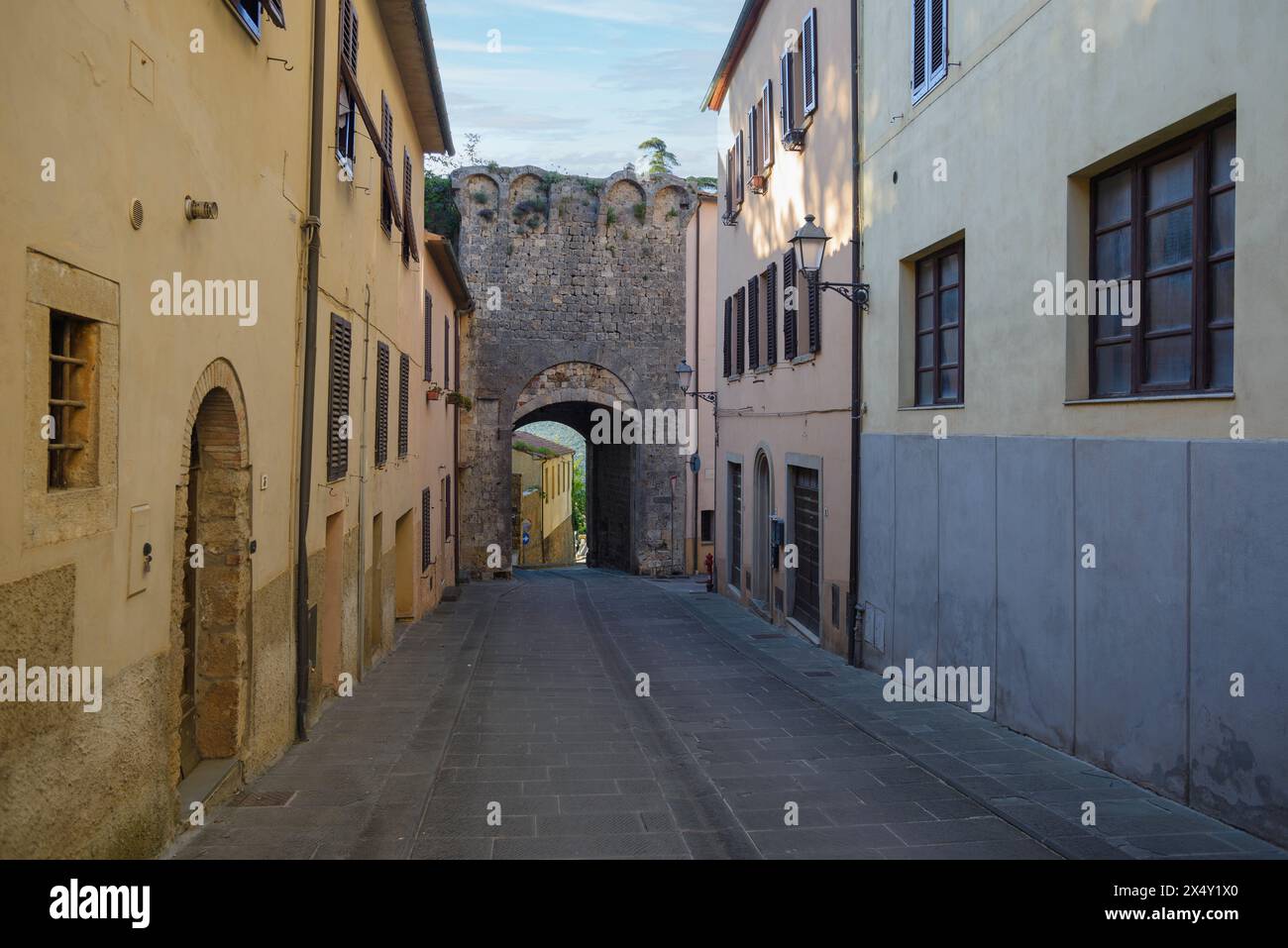 Strada stretta e tranquilla con storico arco in pietra, ingresso alla città di massa Marittima, Grosseto, Italia Foto Stock