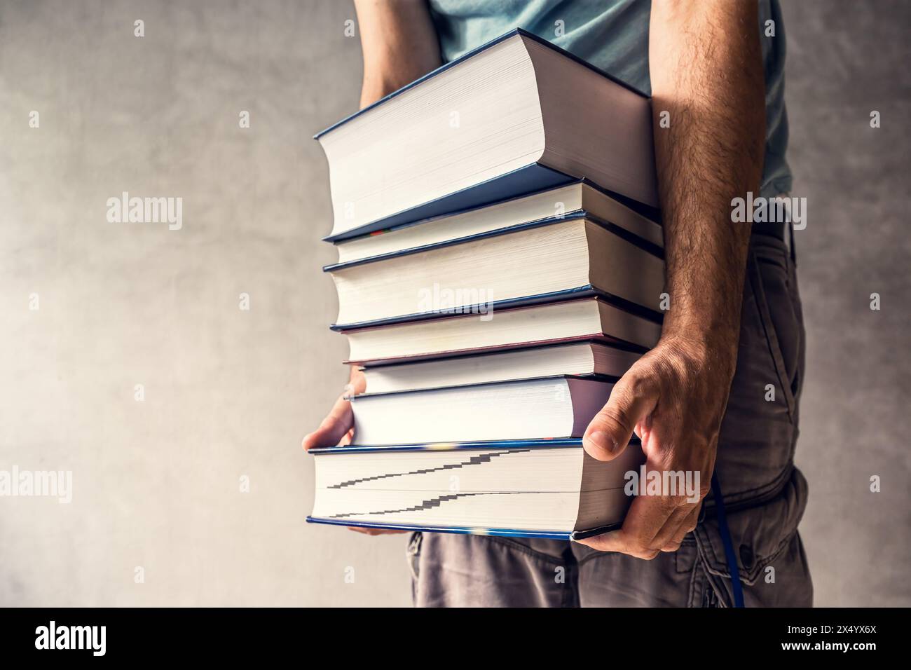 Uomo che porta libri pesanti, che gli richiede di mettere tutta la sua forza nel sollevare la letteratura, focalizzarsi selettivamente Foto Stock