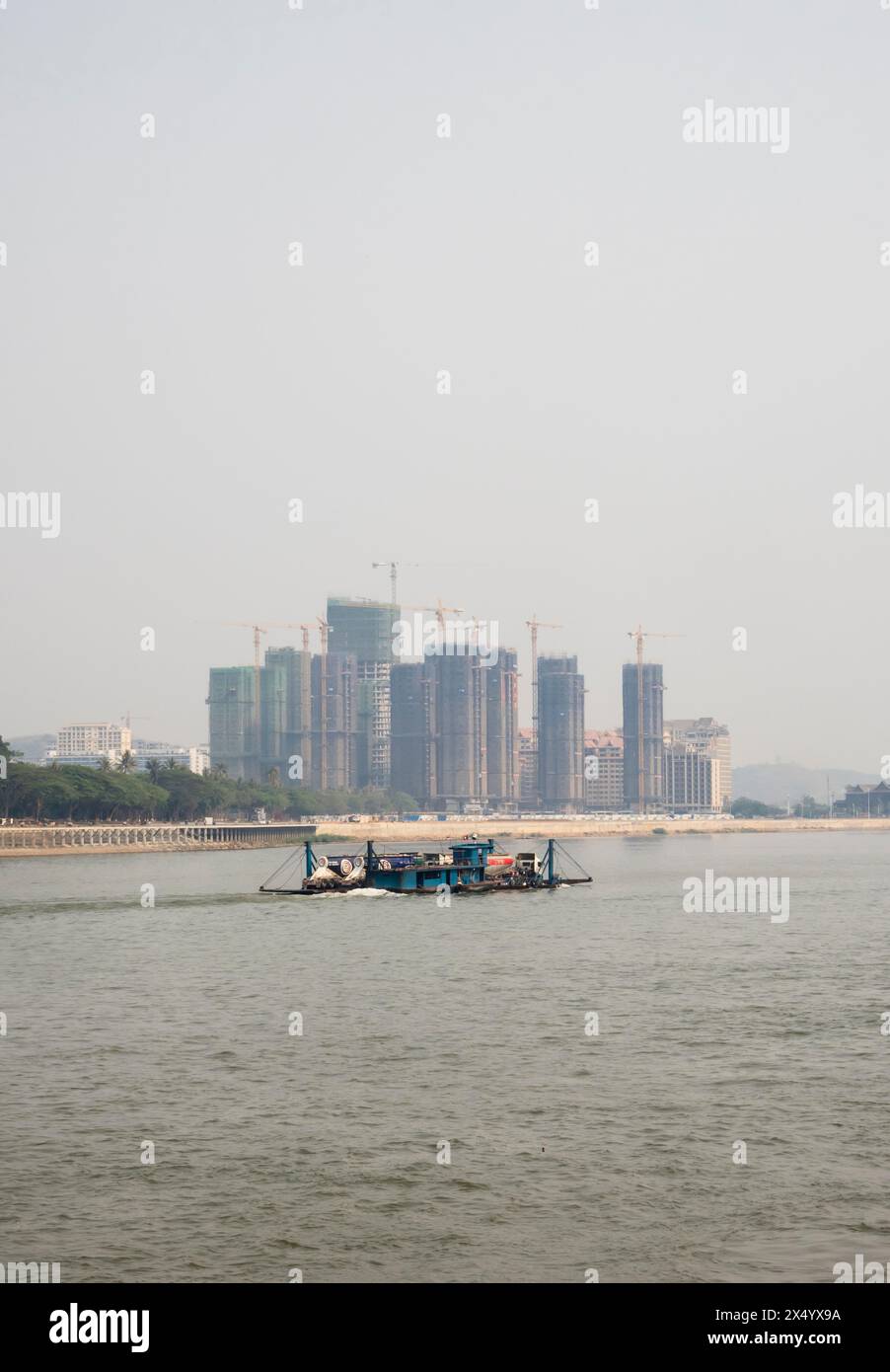 Van Pak Len, Laos - 28 marzo 2024: Una nave cargo passa per edifici residenziali hirise in costruzione sulle rive del fiume Mekong. Foto Stock