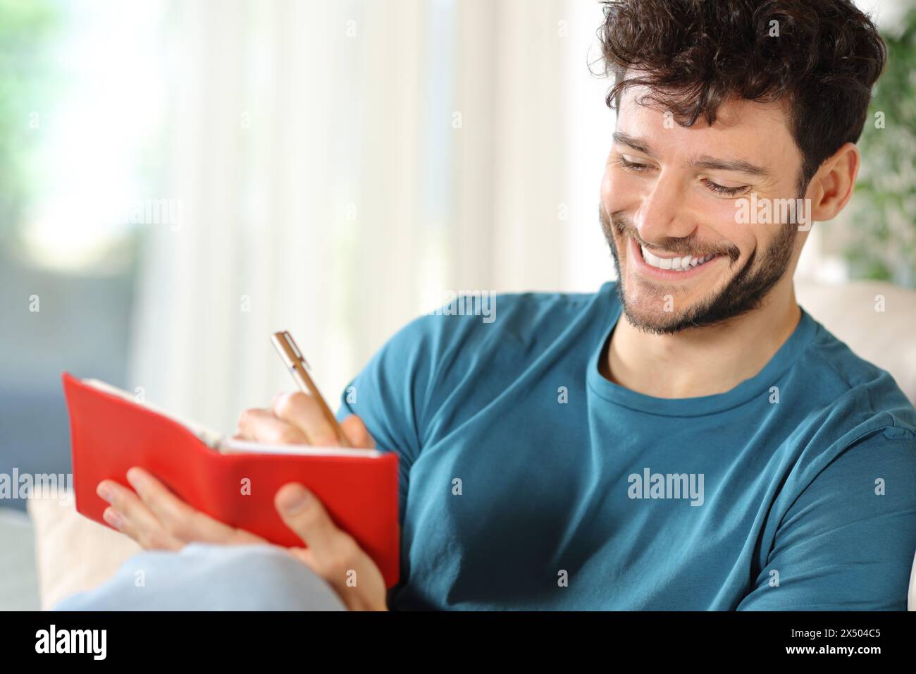 Uomo felice che scrive all'ordine del giorno seduto su un divano a casa Foto Stock