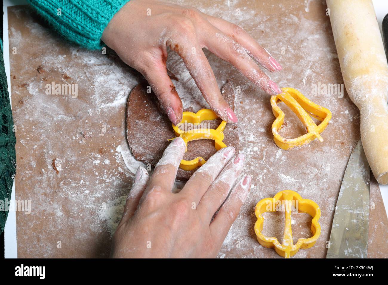 Una donna forma un pan di zenzero usando una muffa di plastica su un impasto arrotolato. La superficie di lavoro è in farina, gli attrezzi si trovano accanto ad essa. Cucinare pan di zenzero. Foto Stock