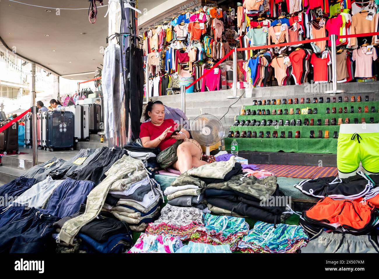 I detentori di stalle del mercato siedono tra gli abiti e i prodotti in vendita sul mercato di Pratunam. Bangkok, Thailandia. Foto Stock