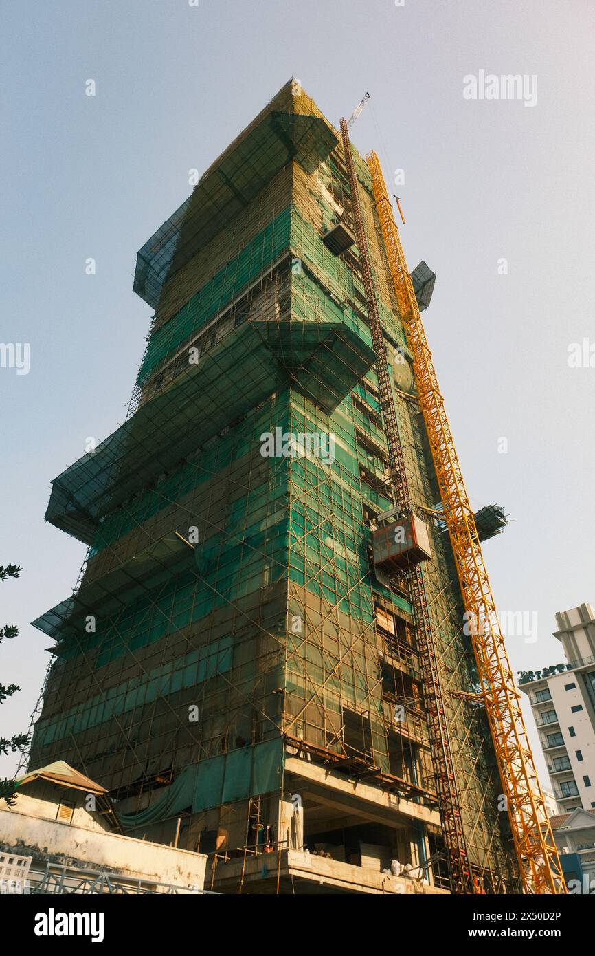 Una scena dinamica si dispiega mentre un grattacielo prende forma nel verde lussureggiante di Phnom Penh, accostato alle strutture improvvisate sottostanti. Foto Stock