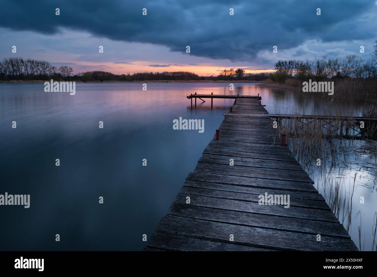 Lungo molo in legno sul lago al tramonto nuvoloso, vista in una serata primaverile Foto Stock