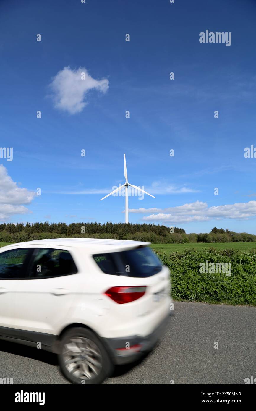 Un'auto bianca che passa davanti a una gigantesca turbina eolica Foto Stock