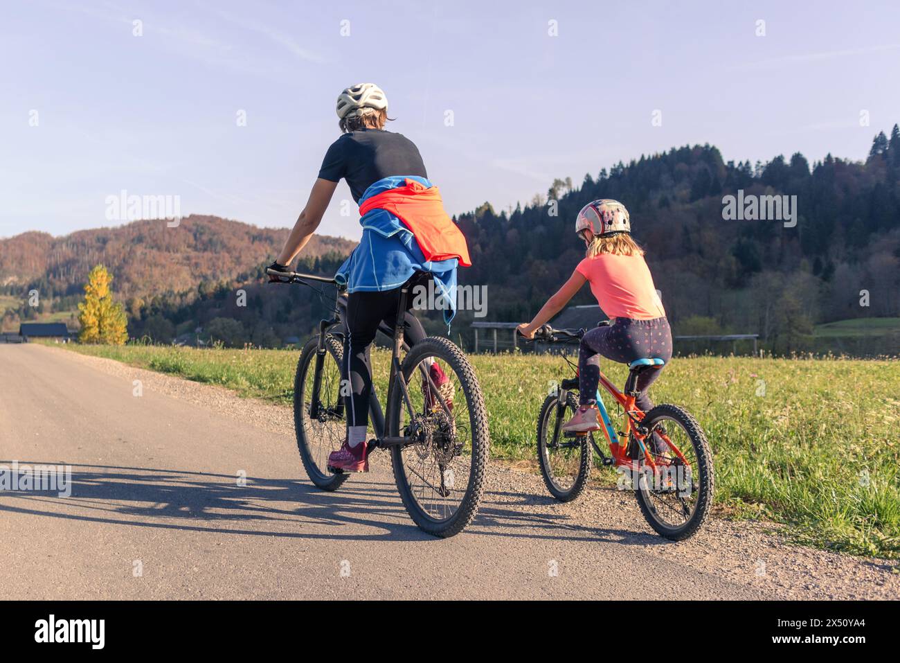 Due ciclisti, una madre con una bambina in bicicletta lungo la strada nella natura rurale. Concetto di svago per famiglie. Foto Stock