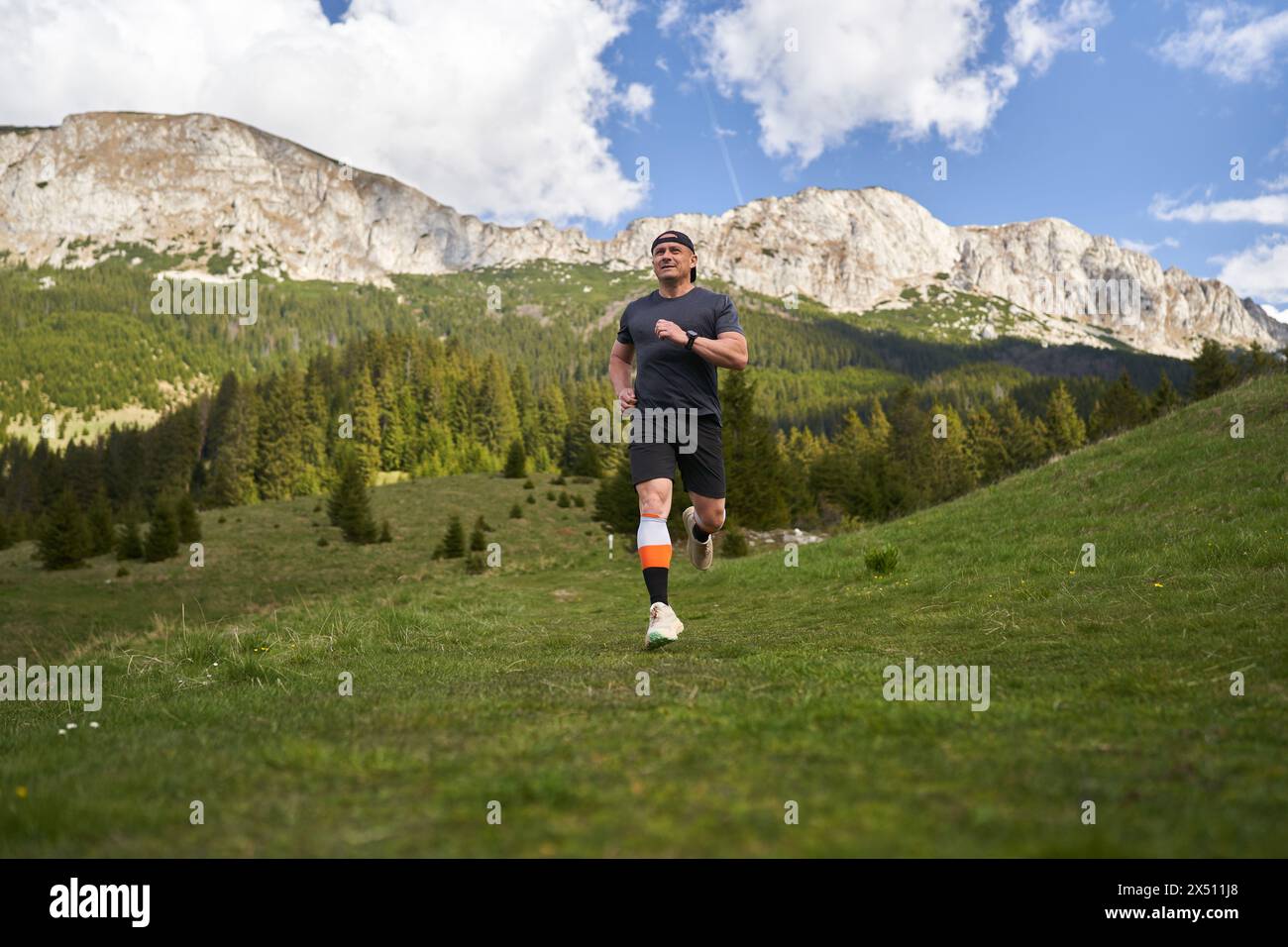 Sentiero uomo maturo che corre ad alta quota in montagna, sull'erba Foto Stock
