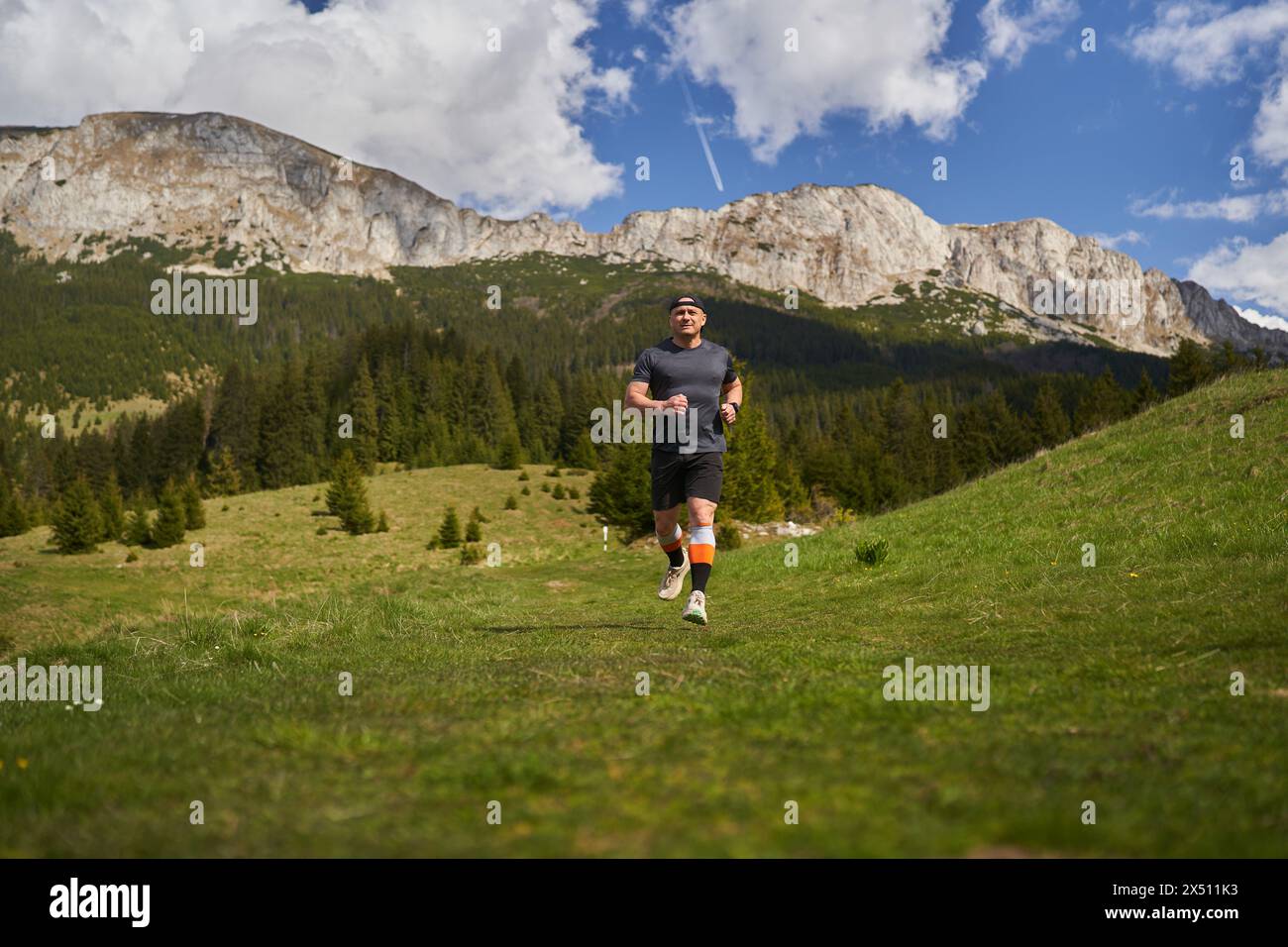 Sentiero uomo maturo che corre ad alta quota in montagna, sull'erba Foto Stock