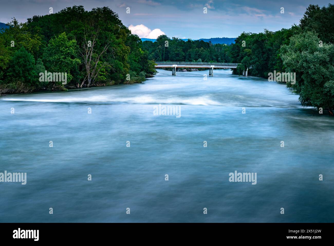 Fiume dopo alcuni giorni di forte pioggia. Acqua levigata con esposizione prolungata. Bellissimi colori blu e bianco che contrastano con il verde degli alberi e. Foto Stock