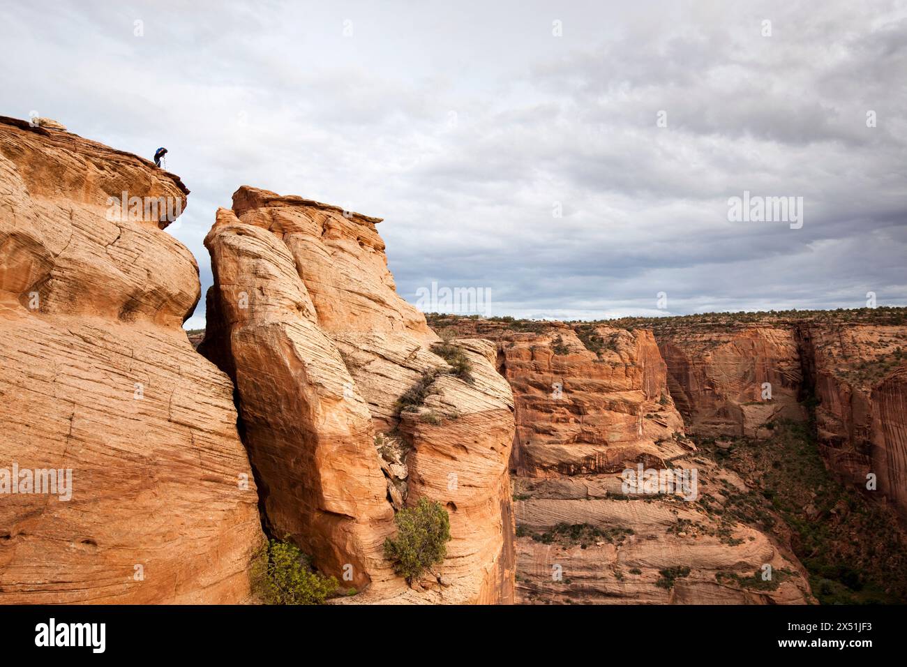 Un fotografo si trova sul bordo di un affioramento roccioso sul bordo del Canyon de Chelly. Foto Stock