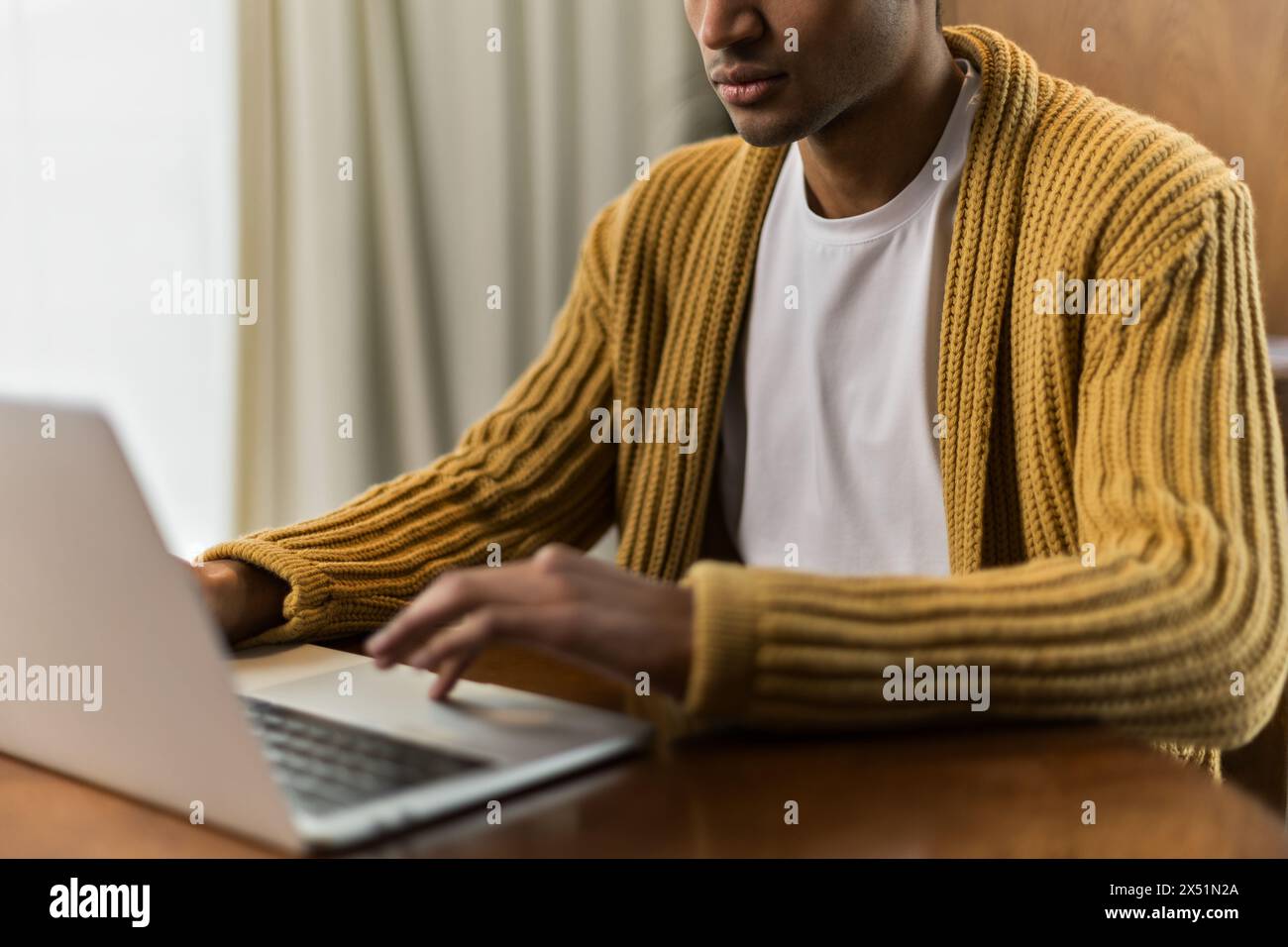 Il giovane latino si siede a un tavolo a lavorare a casa con un computer portatile Foto Stock