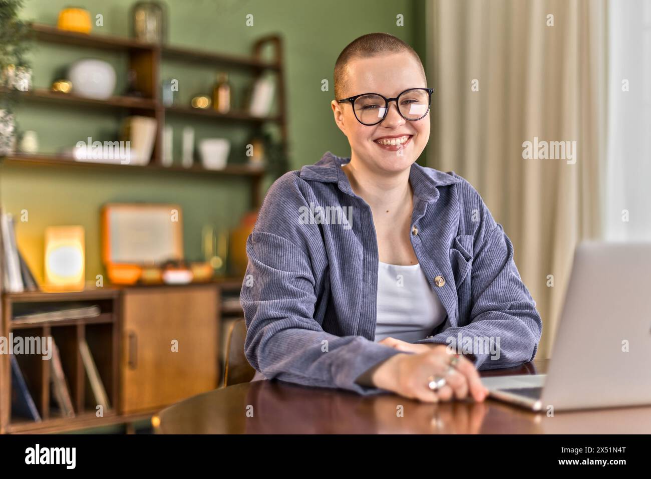 ritrarre una giovane donna calva seduto a un tavolo lavorando da remoto su un notebook Foto Stock