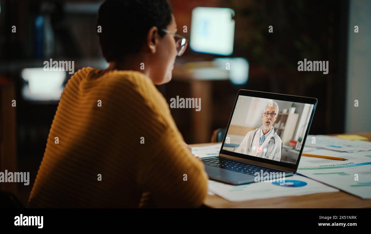Il bellissimo multietnico Latina Manager sta effettuando una videochiamata al suo medico su un laptop in un ambiente ufficio creativo. L'uomo sta parlando con il suo consulente medico su una telecamera dal vivo, chiedendo di salute. Foto Stock