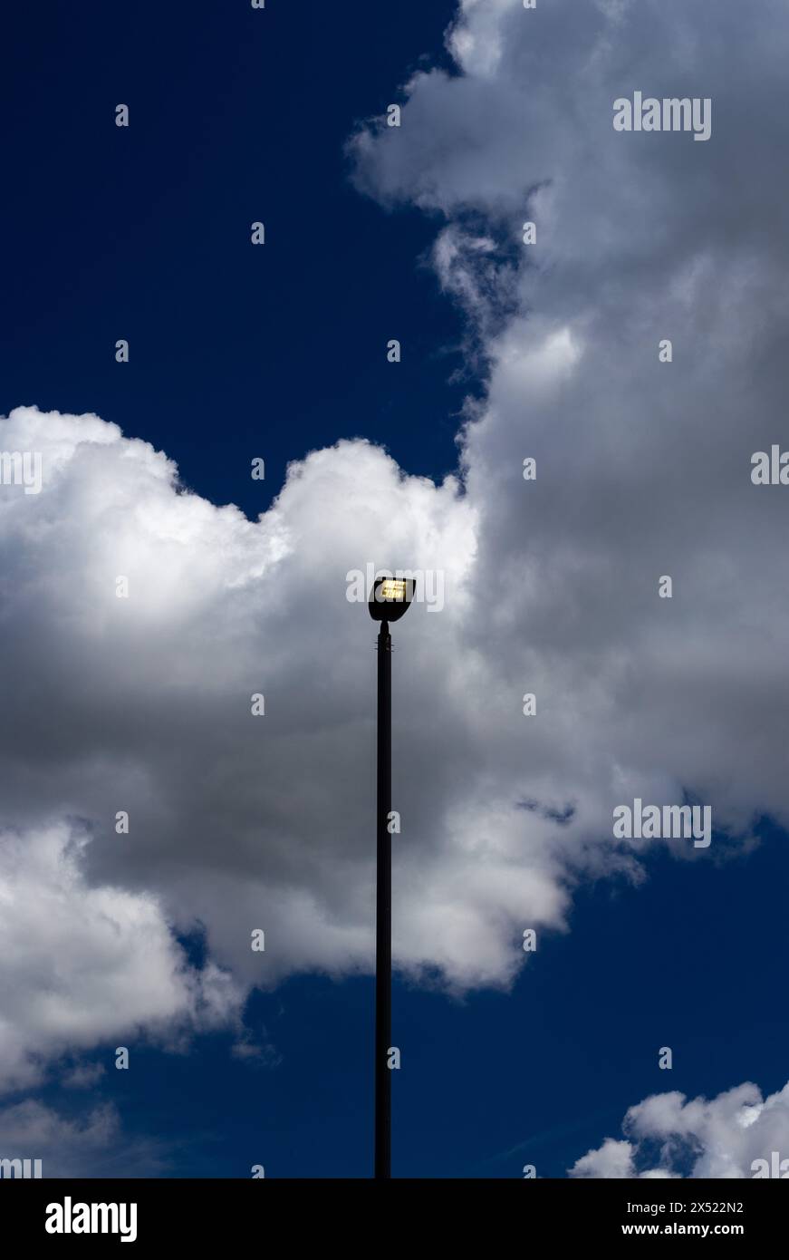 Le luci a LED si accendono di giorno con un cielo azzurro e nuvole bianche. I piedistalli alti per lampade sono verticali sia in verticale che in orizzontale. Spazio per una copia Foto Stock