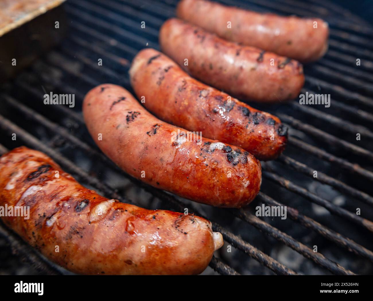 Cinque salsicce grigliate su un barbecue all'aperto con segni di carattere visibili. Un'immagine appetitosa ideale per cibi, grigliate, barbecue e contenuti a tema estivo Foto Stock