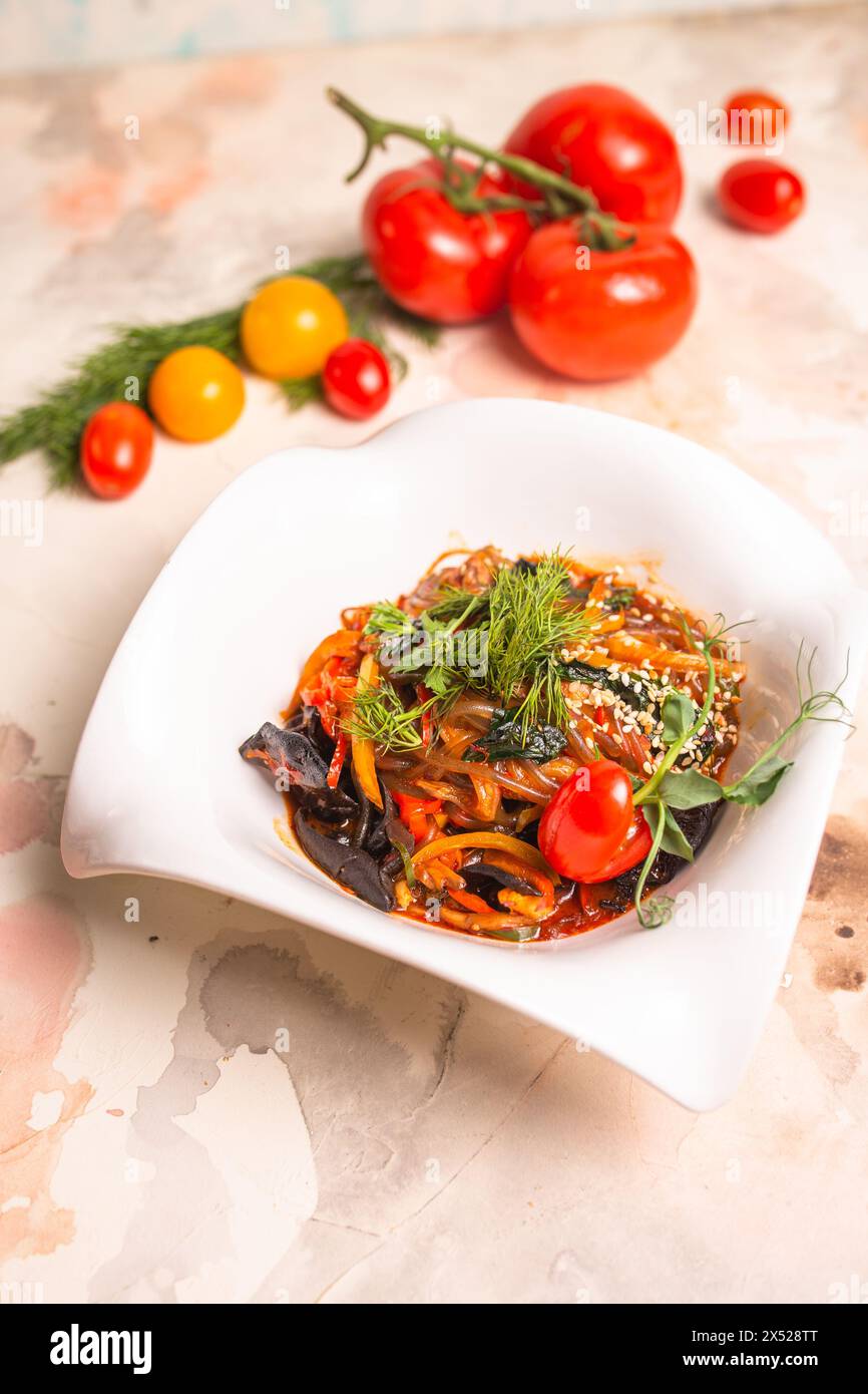 Un pasto delizioso e salutare di Japchae, realizzato con spaghetti di patate dolci, verdure, e una salsa salata, guarnita con pomodori e aneto Foto Stock