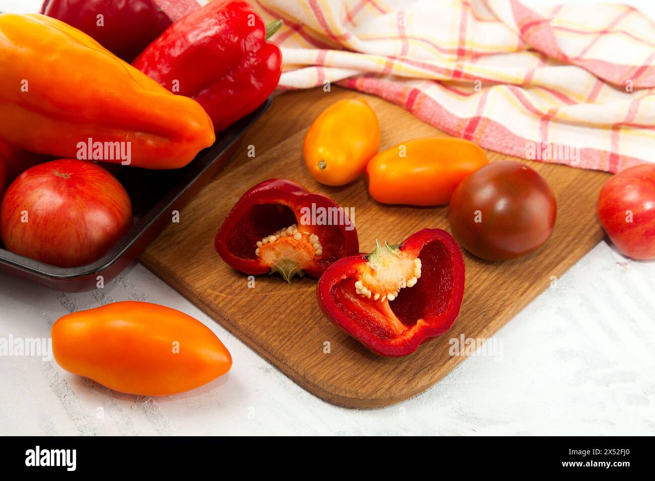 Ciotola con verdure su tagliere con assort di diversi pomodori succosi interi e peperoni su fondo di legno bianco con cucina rossa Foto Stock