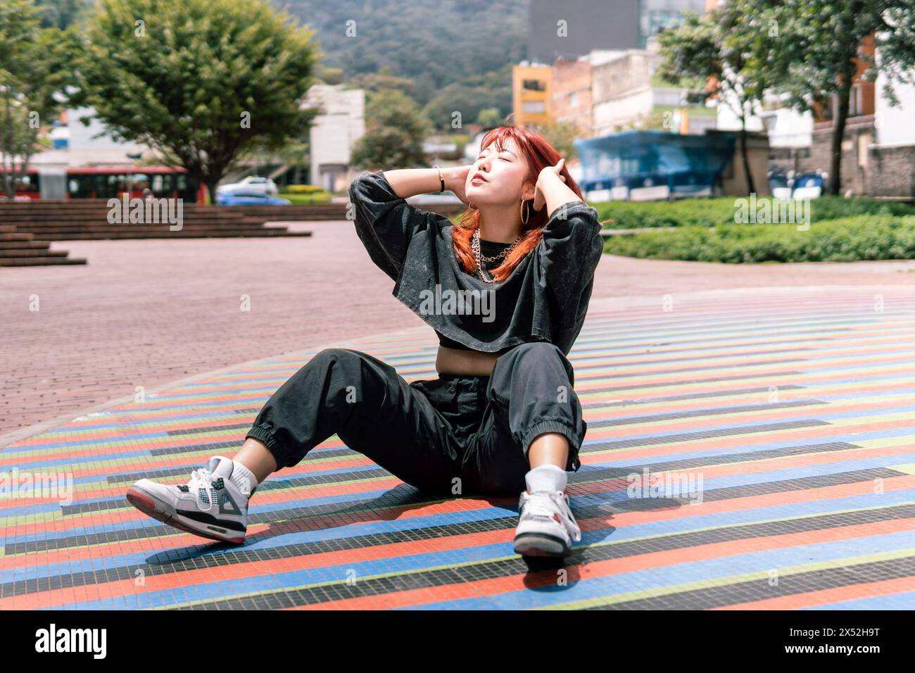 Donna coreana serena con capelli rossi seduta in relax su una colorata piazza della città Foto Stock