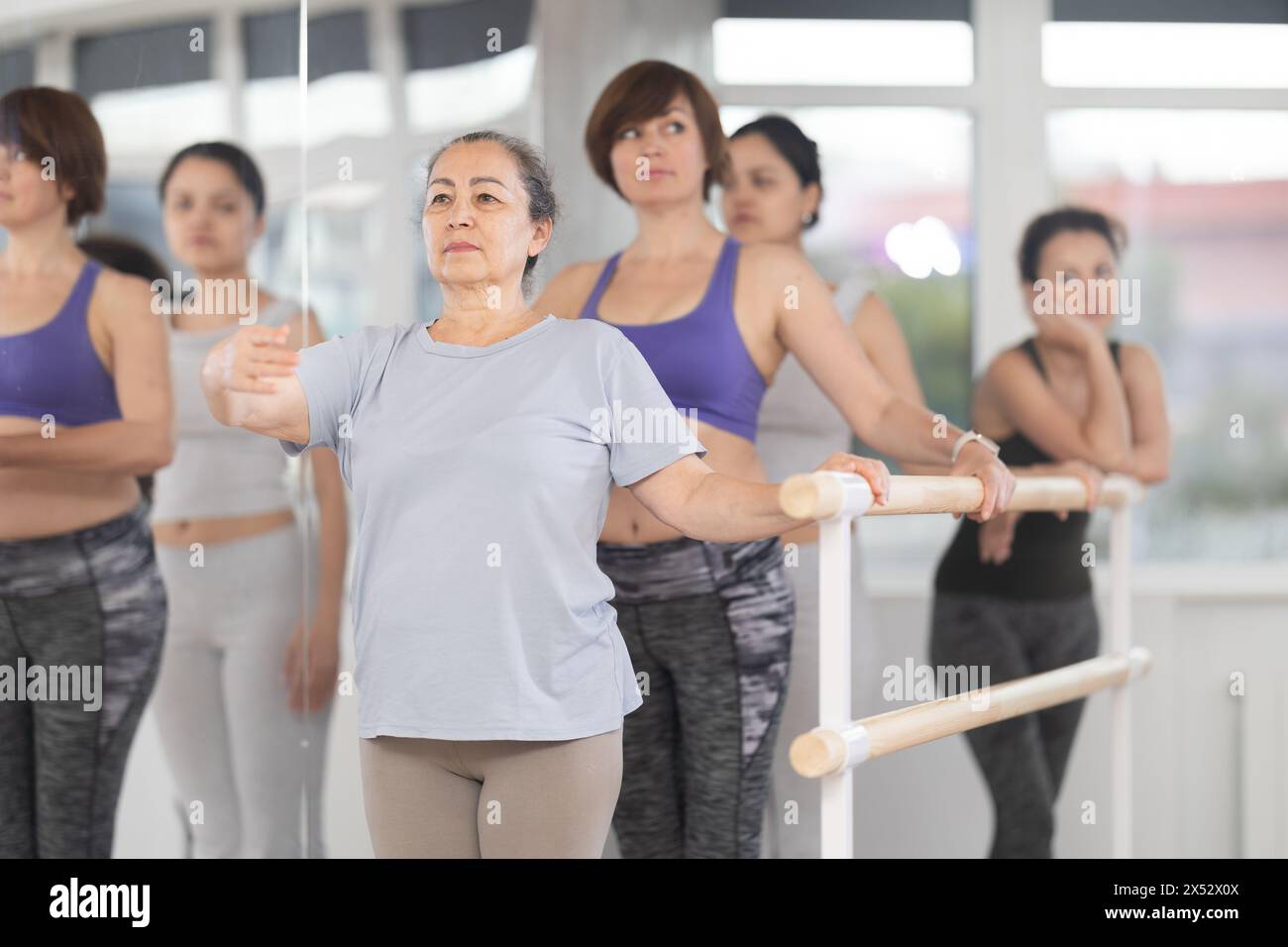 Donna anziana che impara la prima posizione di balletto a barre in classe di gruppo Foto Stock