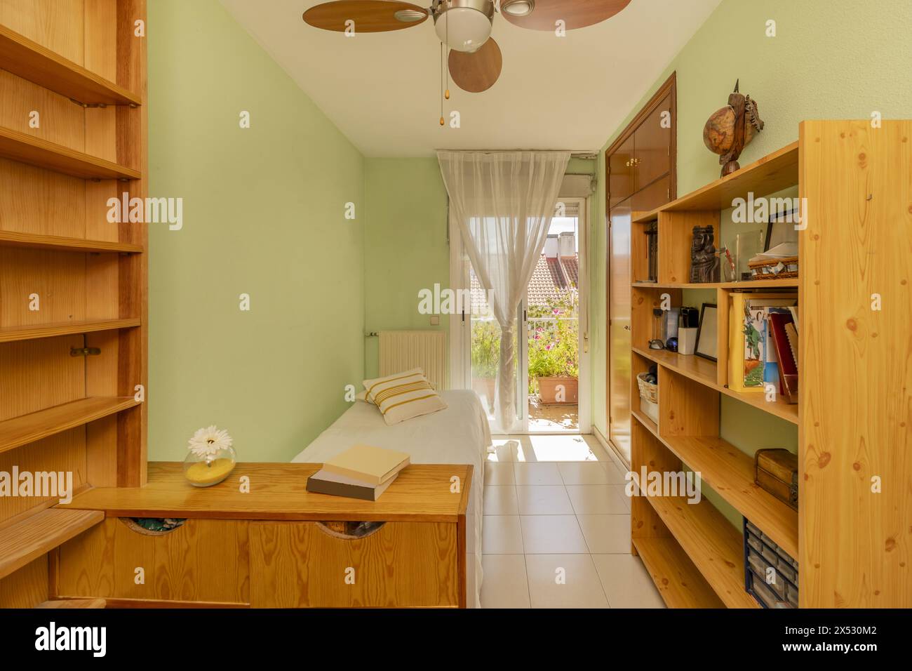 Camera con letto singolo, scaffali in legno di pino e accesso a una terrazza con pentole piene di fiori Foto Stock