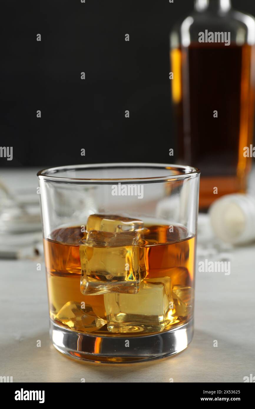 Dipendenza da alcol. Whisky con cubetti di ghiaccio in vetro su un tavolo bianco Foto Stock