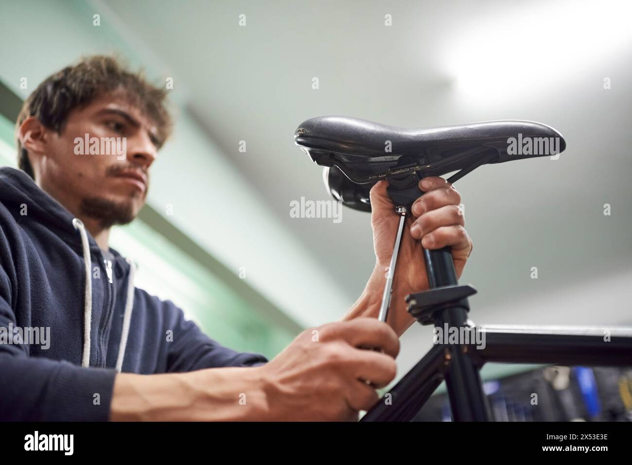 Giovane latino che regola una sella di bicicletta nella sua officina come parte di un servizio di manutenzione. Persone vere al lavoro. Composizione con messa a fuoco selettiva Foto Stock