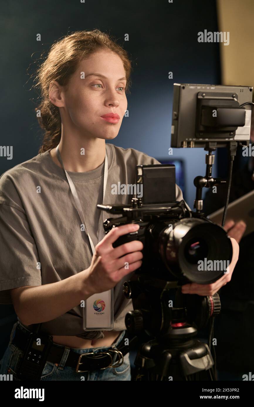 Ritratto verticale di una camerawoman caucasica sorridente che opera sul set durante la produzione video Foto Stock