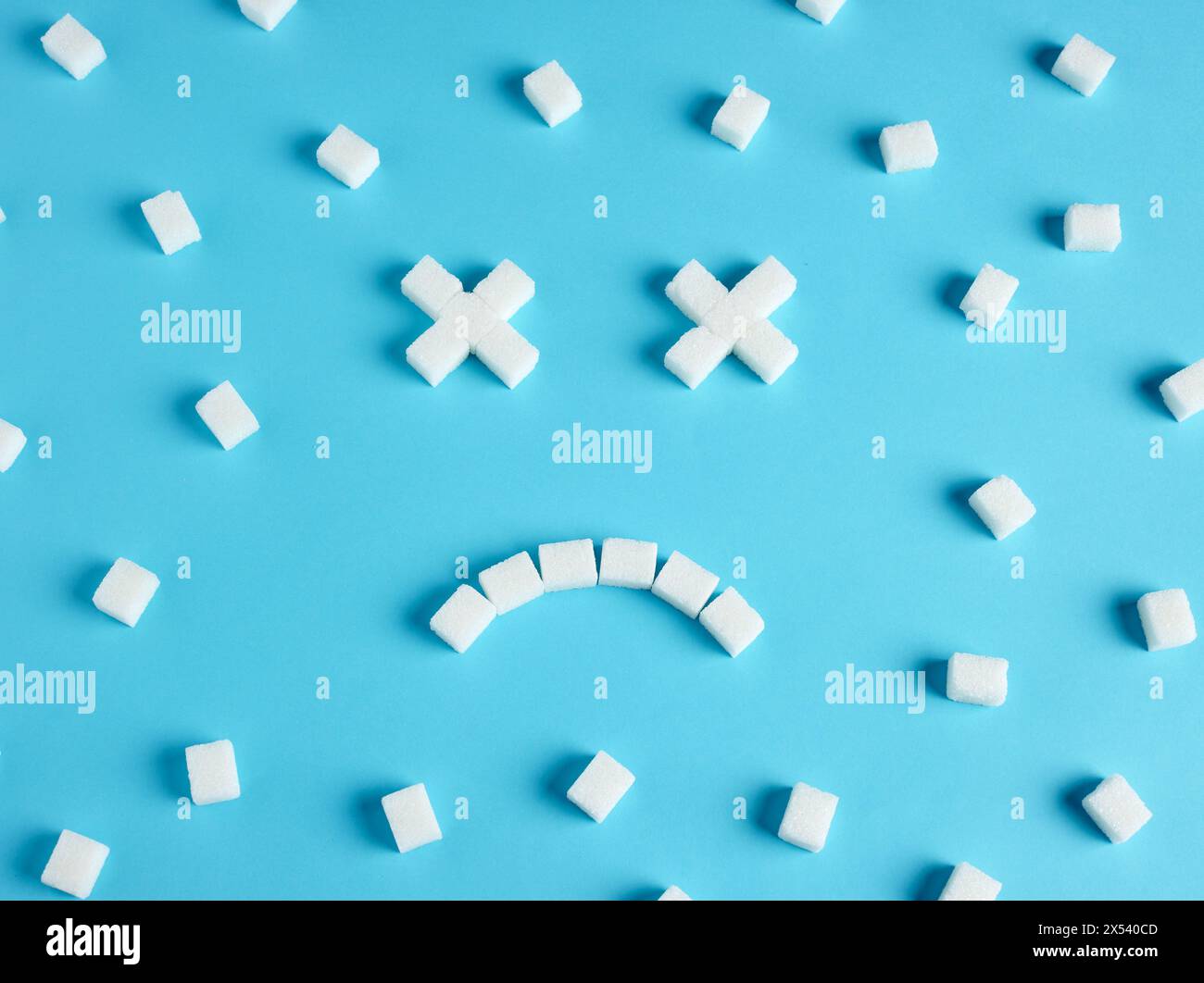 Consumo eccessivo di zucchero. Pericoli di un eccessivo apporto di zucchero. Rischio di diabete e problemi di salute. Faccia sorridente di emoticon morta fatta di cubetti di zucchero su blu Foto Stock