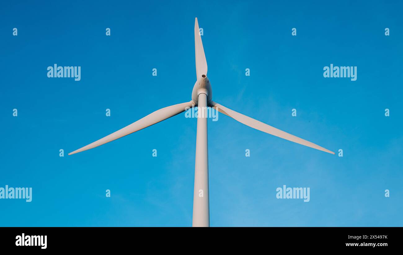 Una turbina eolica è alta nel cielo, con il cielo blu dietro di essa Foto Stock