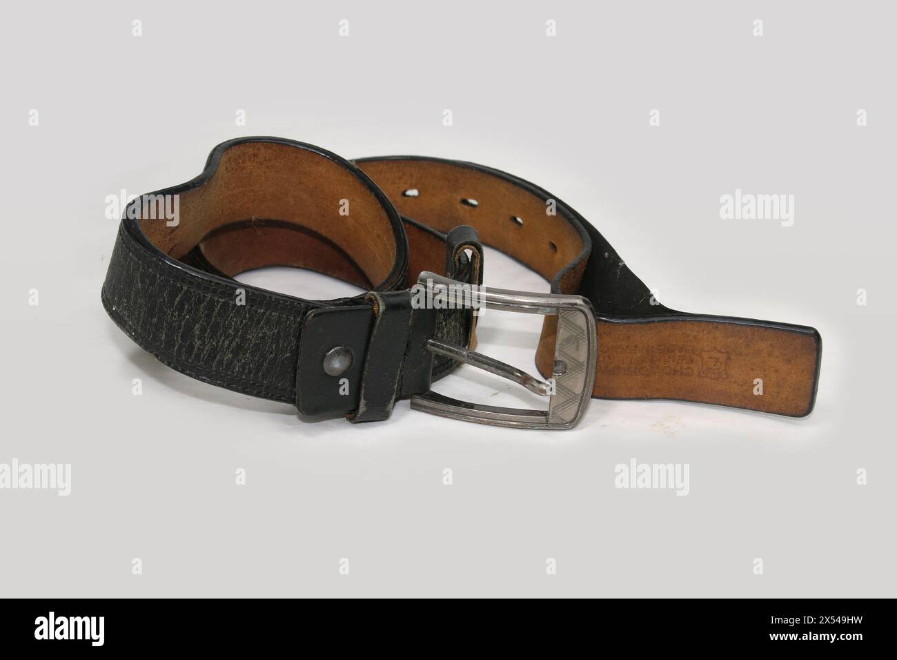 Cintura in pelle nera usata e vecchia con fibbia isolata su sfondo bianco. Cintura in pelle nera arrotolata invecchiata con fibbia in metallo. Foto Stock
