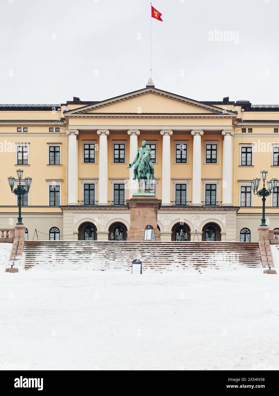 Facciata del palazzo reale neoclassico di Oslo in inverno con volo standard reale norvegese e statua equestre del re Carl Johan, Oslo, Norvegia Foto Stock