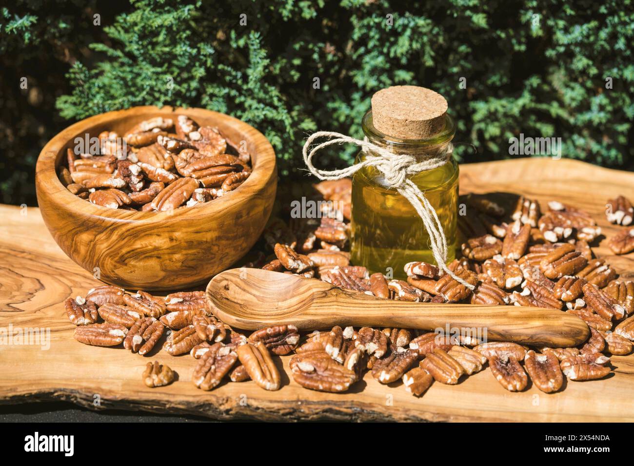 Pecan (Carya illinoiensis, Carya pecan), pecan incrinate in una ciotola di legno con un cucchiaio di legno e una bottiglia di olio di noci Foto Stock