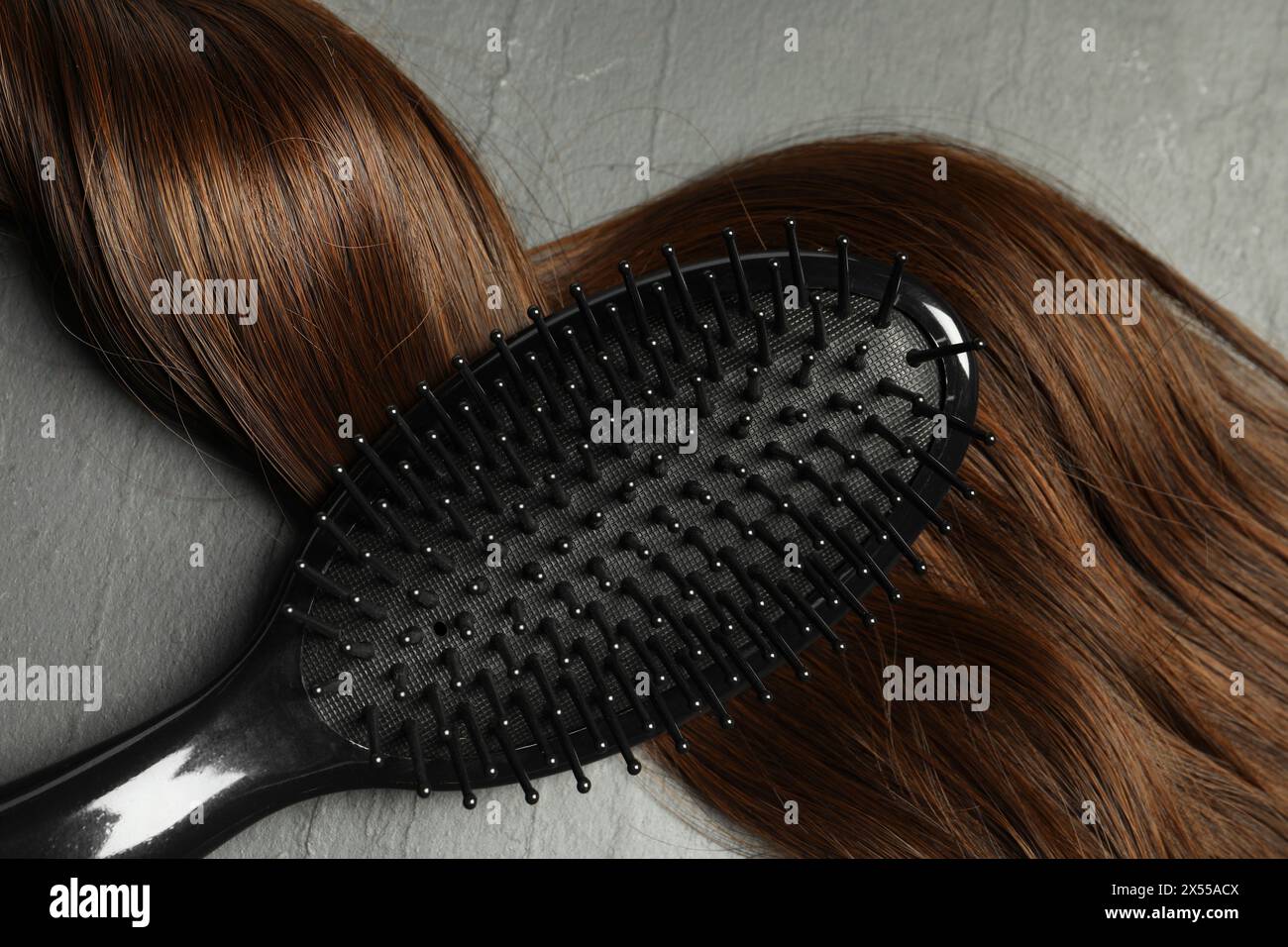 Spazzola elegante con ciocche di capelli marroni su tavolo grigio scuro, vista dall'alto Foto Stock