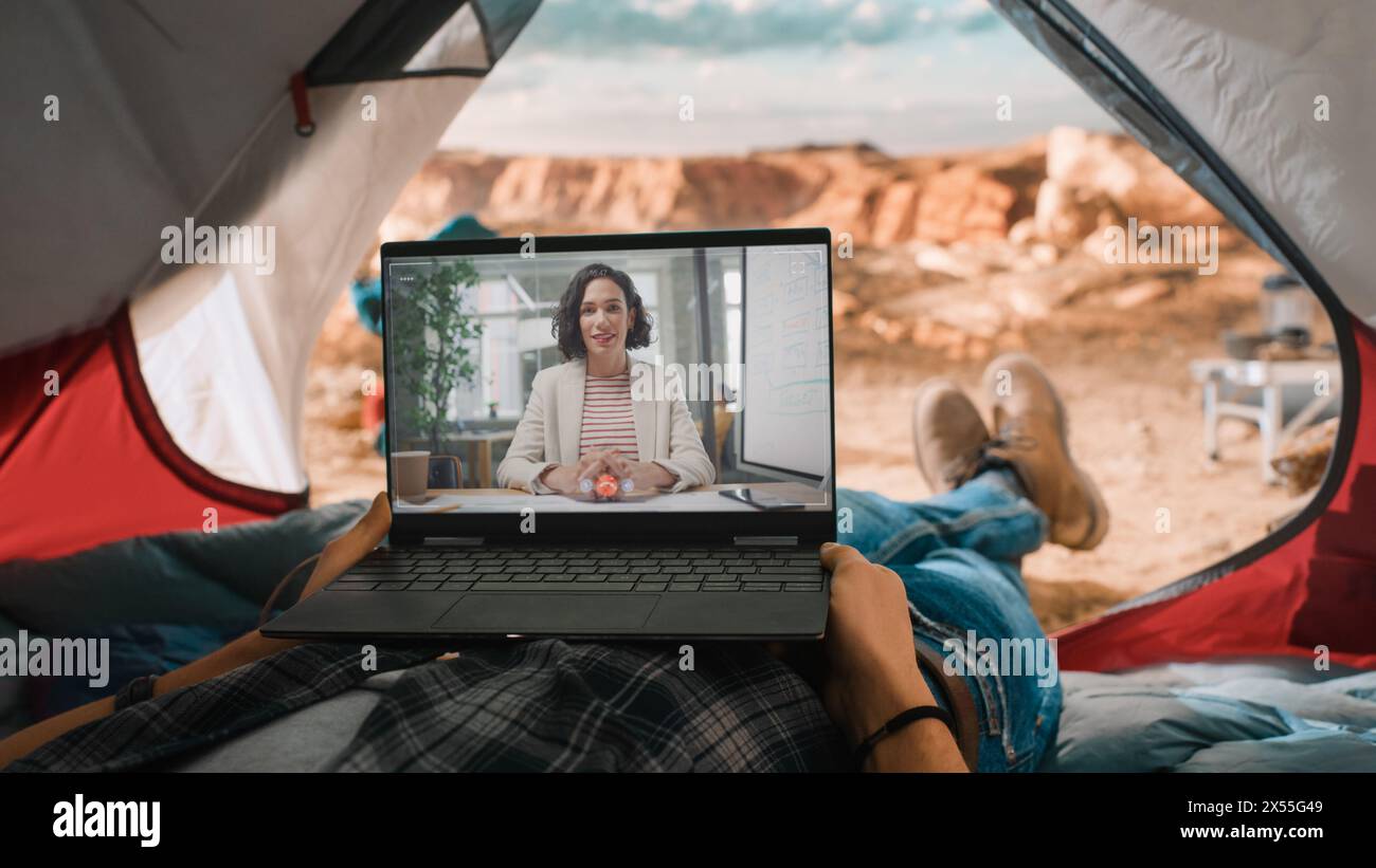 POV di un turista che effettua una videochiamata con un amico o un collega sul computer portatile. Viaggiatore che riposa in una tenda sulla cima di una montagna rocciosa. Avventuroso escursionista che vive nella natura. Foto Stock