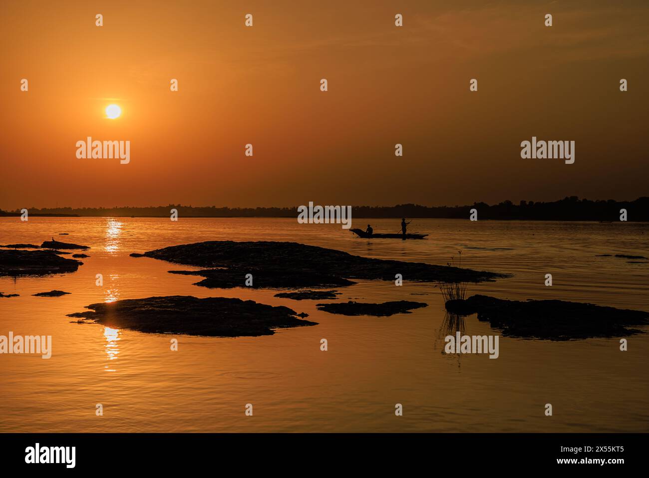 tranquilla scena fluviale al tramonto mentre una barca da pesca in legno passa accanto a piccole isole del fiume sacro a maheshwar in india Foto Stock