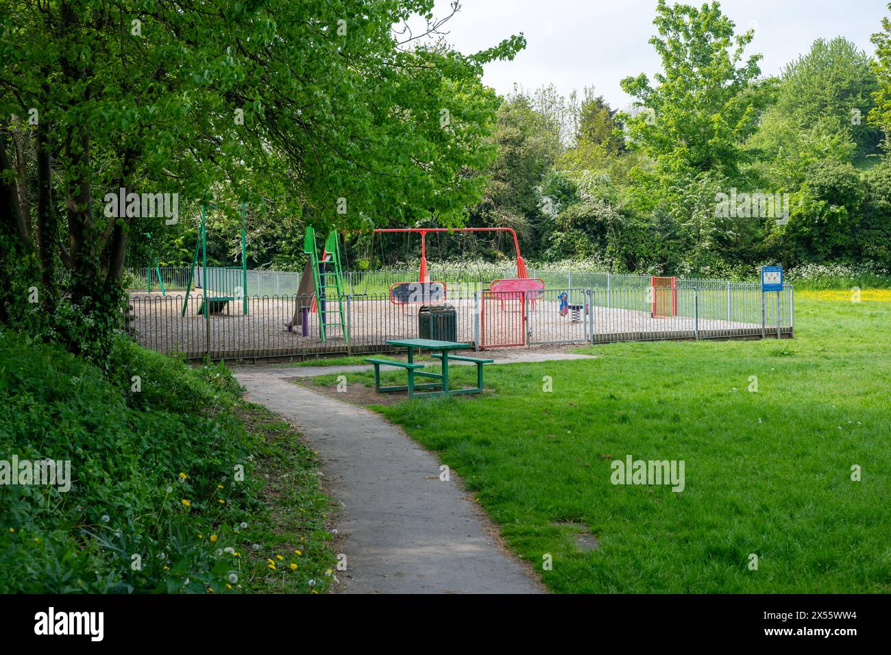 Un piccolo, colorato e vuoto parco giochi per bambini circondato da alberi, arbusti e fiori primaverili. Foto Stock