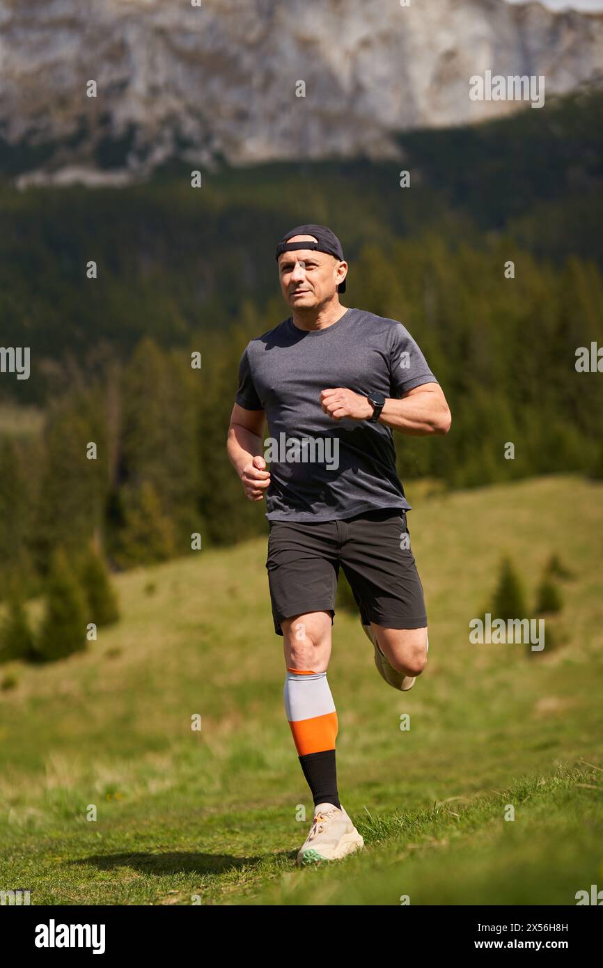Trail runner in una corsa con montagne dietro su un prato Foto Stock