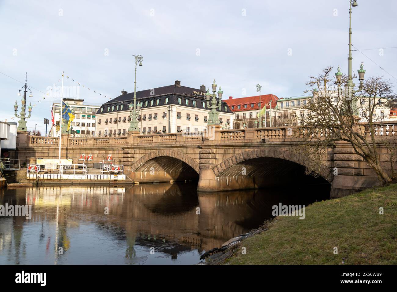 Goteborg, Svezia - 22 gennaio 2022: Ponte in pietra con due archi e grandi lampade in rame. Edifici sullo sfondo. Persone visibili che attraversano il ponte Foto Stock