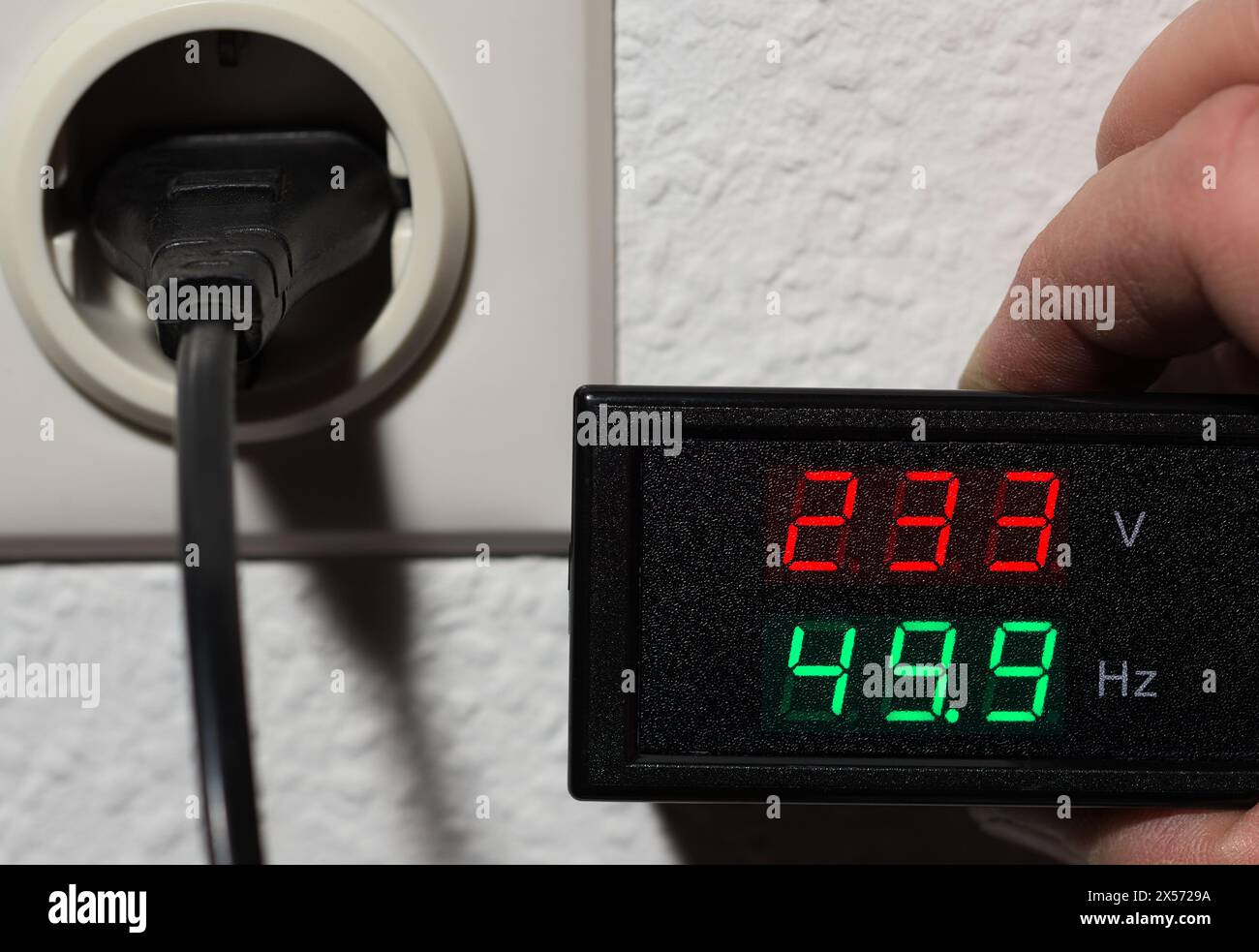 Controllo della tensione e della frequenza in hertz del test di qualità dell'alimentazione della rete elettrica con il voltmetro sulla presa Foto Stock