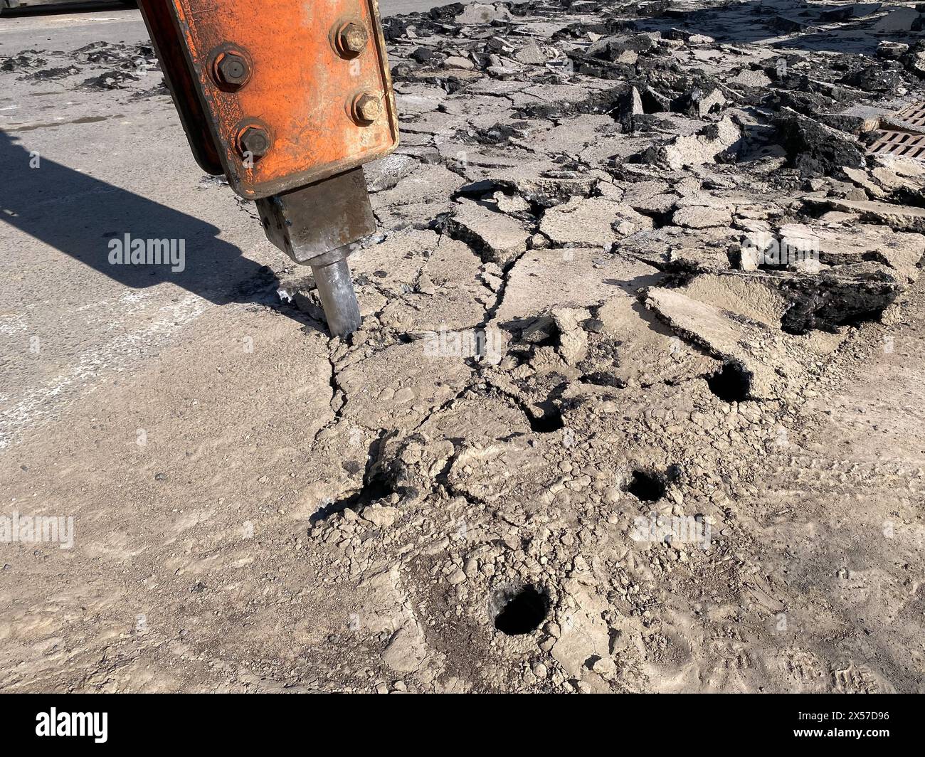 La macchina pesante con martello demolitore sta rompendo l'asfalto su una strada urbana, concentrandosi in modo selettivo. Il funzionamento della perforazione del fondo stradale Foto Stock