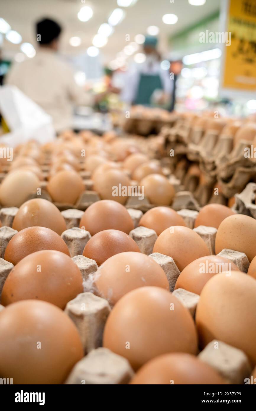 Uova di pollo su vassoi in vendita in un supermercato con acquirente e personale sullo sfondo Foto Stock
