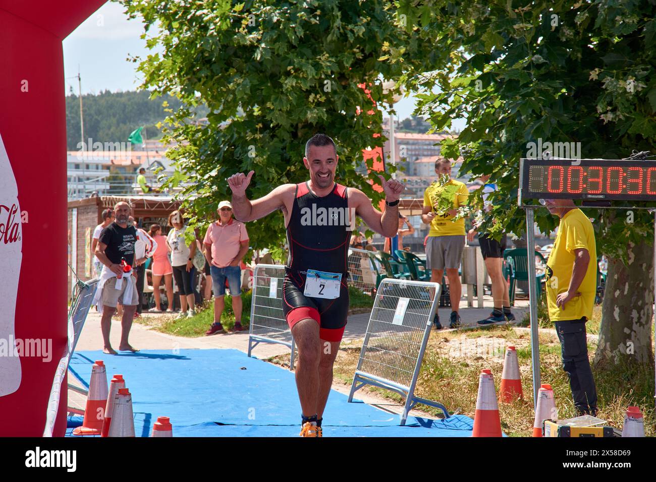 Sabaris, Baiona, Pontevedra, Spagna; 15 luglio, 2023; Un atleta di triathlon raggiunge il traguardo sorridendo e alzando le braccia nel popolare Ladeira tri Foto Stock