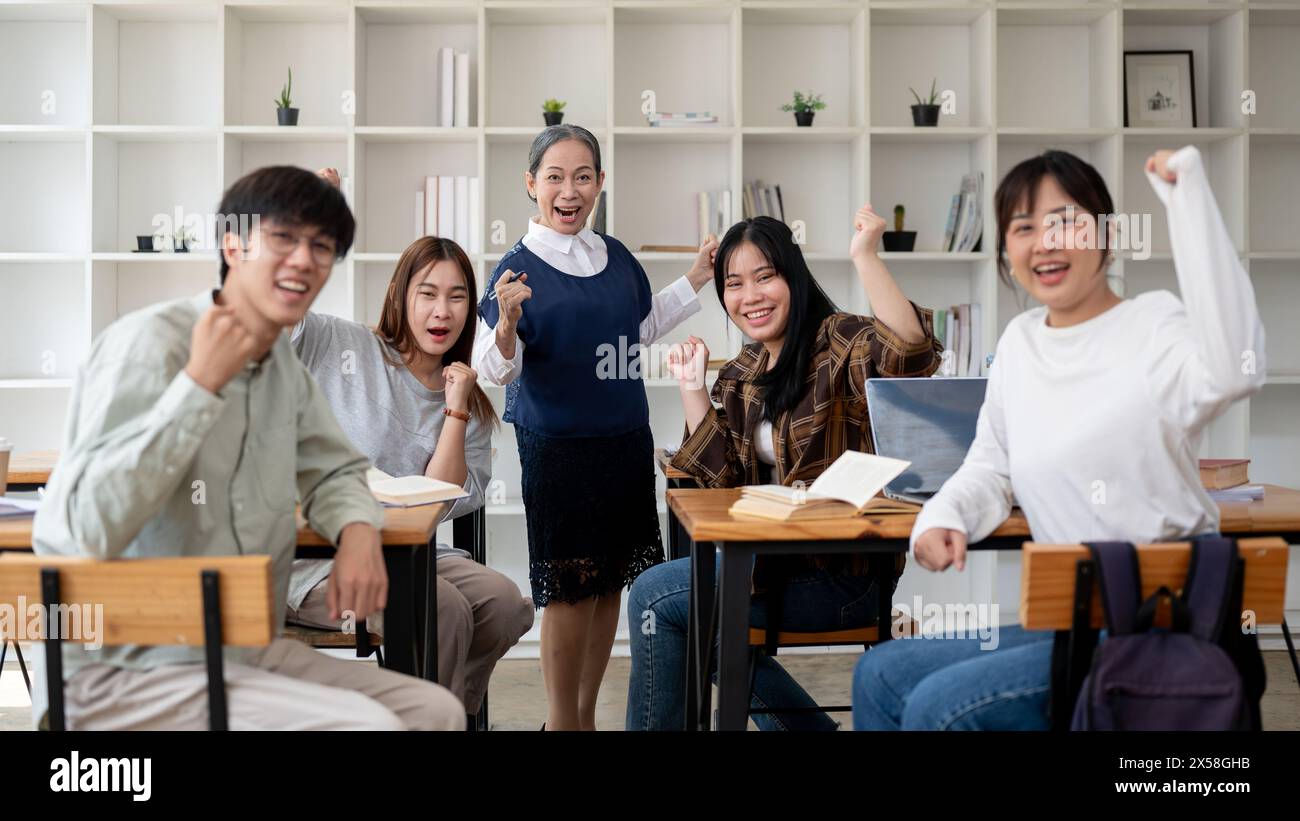 Un'allegra insegnante asiatica matura o professoressa con i suoi studenti che mostrano il pugno, la posa trionfale, sorridendo alla telecamera, celebrando le buone notizie Foto Stock