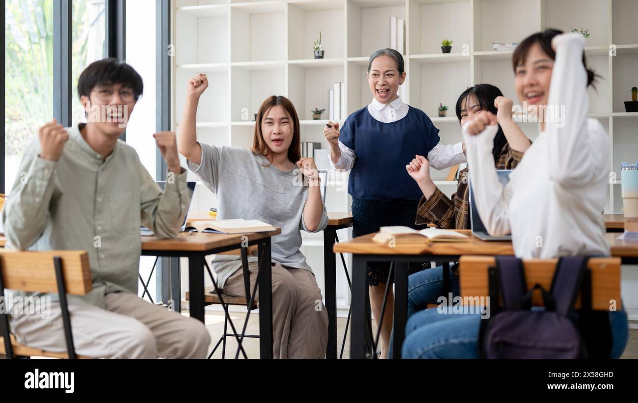 Un'allegra insegnante asiatica matura o professoressa con i suoi studenti che mostrano il pugno, la posa trionfale, sorridendo alla telecamera, celebrando le buone notizie Foto Stock