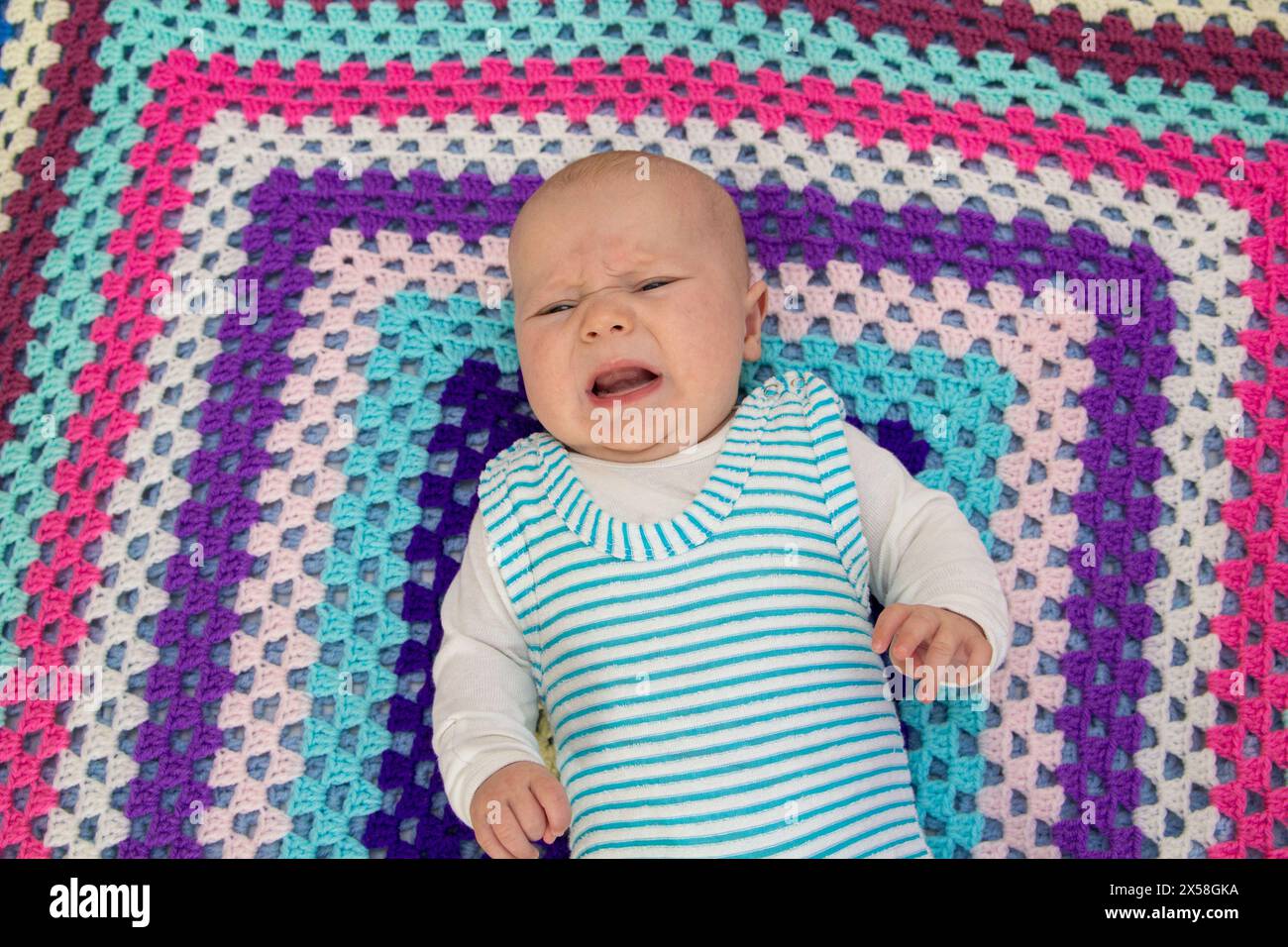 il neonato piange su una coperta a maglia di colori diversi Foto Stock